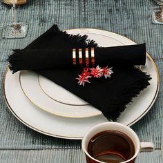 a table setting with black napkins and flowers on the placemat, next to a cup of coffee