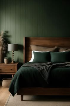 a bed with green sheets and pillows in a dark room next to a lamp on a dresser