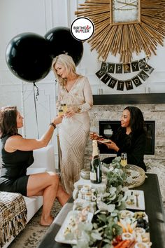 two women sitting at a table in front of a fireplace with black and white balloons