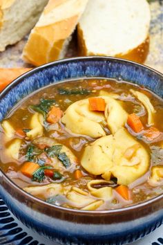 a bowl of soup with dumplings and carrots next to bread on a table