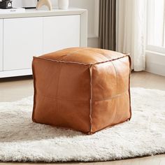 a square leather ottoman sitting on top of a white rug in front of a window