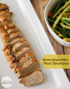 sliced pork tenderloin on a white platter with green beans and asparagus