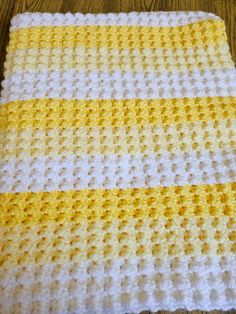 a yellow and white crocheted blanket on a wooden floor