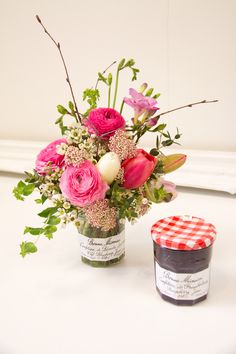 a vase filled with pink flowers and greenery next to a jar of jam on a table