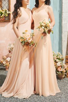 two women standing next to each other in long dresses with flowers on the side and one holding a bouquet