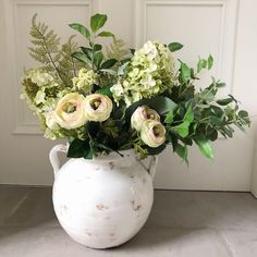 a white vase filled with lots of green and white flowers on top of a table