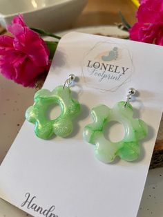 two green flower shaped earrings sitting on top of a white card next to pink flowers