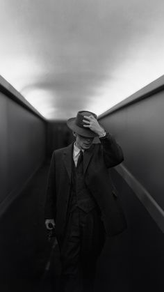 a man in a suit and hat walking down a hallway with his hand on his head