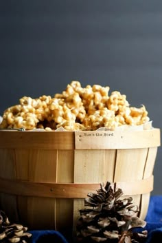 a wooden basket filled with popcorn next to pine cones