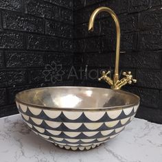 a black and white bowl with gold faucet on the top is shown in front of a brick wall