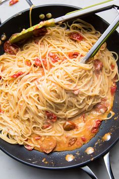 a pan filled with spaghetti and sauce on top of a stove burner next to utensils