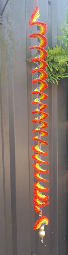 a colorful wind chime hanging from the side of a metal wall next to a potted plant