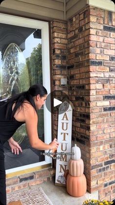 a woman is opening the front door of a house with an autumn sign in front of her