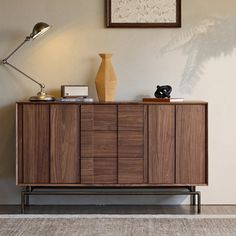 a wooden cabinet with a lamp on top of it next to a rug and wall