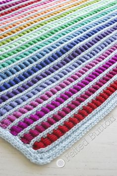 a multicolored crocheted rug is laying on a white wooden table top