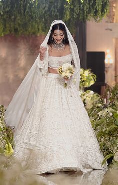 a woman in a white wedding gown and veil walking down the runway with her bouquet