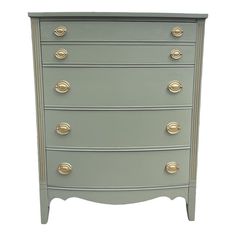 a grey chest of drawers with gold knobs on the top and bottom, against a white background