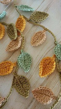 crocheted leaves are hanging on a wooden surface with chains attached to them, all in different colors