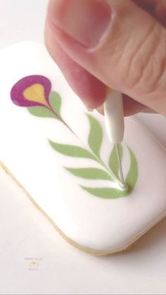 a hand holding a small white object with a flower painted on it's side