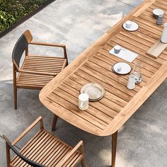 a wooden table with plates and cups on it, next to two chairs that are facing each other