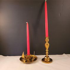 two gold candles with red candlesticks on white table cloth in front of black wall