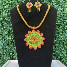 a necklace and earring set on display in front of a green bush with leaves