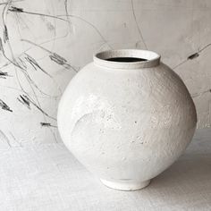 a white vase sitting on top of a table next to a wall with dry grass