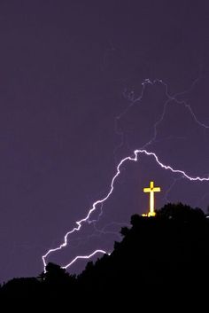 a cross on top of a hill with lightning in the background