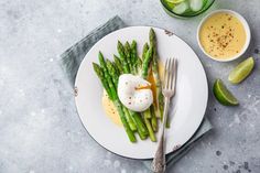 asparagus, eggs and sauce on a white plate next to two glasses of lemonade