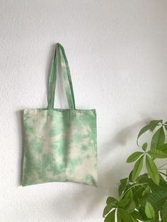 a green and white tote bag hanging on a wall next to a potted plant