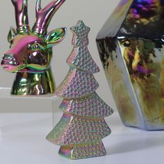 two shiny christmas trees in front of a silver vase with a deer head on it