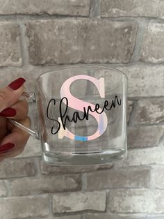 a person holding up a glass mug with the letter s on it in front of a brick wall