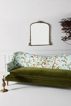 a green couch sitting in front of a mirror on a wall next to a table