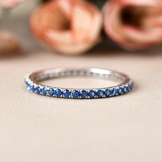 a blue diamond ring sitting on top of a white table next to pink flower petals