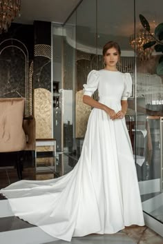 a woman standing in front of a glass door wearing a white dress with puffy sleeves