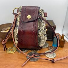 Looking for a stylish storage solution for your dice? Coin pouch for your Larp costume or D&D cosplay? This handcrafted leather bag might just be for you. Mahogany Brown hand stained vegtan leather main band with tan braided detail, and Golden metallic snake print soft leather circle body section.  Brass coloured metalwork including a press popper to the front, eyelets on all the drawstring holes, 2 D-rings, and a deaths head hawk moth charm. Size: approximately 130mm tall and wide Images show t Steampunk Leather Bag For Everyday Use, Brown Hand Tooled Pouch, Vintage Handmade Leather Pouch, Handmade Vintage Leather Pouch, Vintage Brown Leather Pouch, Vintage Handmade Brown Pouch, Handmade Brown Vintage Pouch, Brown Leather Hand-tooled Pouch, Hand Tooled Brown Leather Pouch