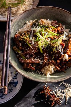 a bowl filled with rice and meat on top of a table next to chopsticks