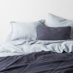 an unmade bed with blue sheets and pillows