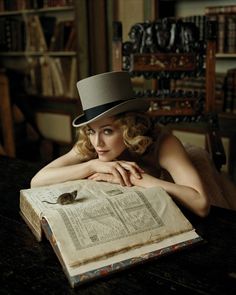 a woman wearing a top hat sitting at a table in front of an open book