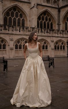 a woman in a wedding dress standing on a stone floor with an old building in the background