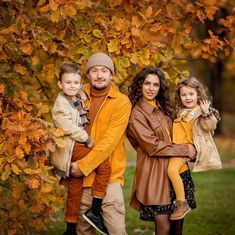 a man and two children are posing in front of a tree with fall leaves on it