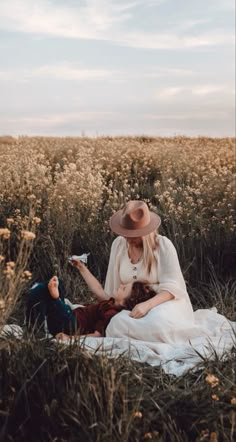 a woman in a white dress and hat sitting next to a man on a field