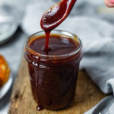 a spoon full of bbq sauce being poured into a jar