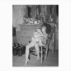 a woman sitting in a chair holding a baby next to a dresser with jars on it