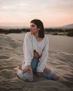 a woman is sitting in the sand with her hands on her hips and looking off into the distance