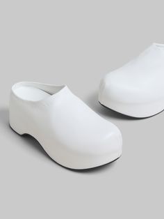 Chunky clog sabot with lightweight wooden platform sole, covered entirely in sleek nappa leather. Subtly embellished with debossed Marni lettering along the edge. Leather insole and ribbed rubber outsole. White Platform Clogs With Round Toe, Modern Synthetic Clogs With Round Toe, White Platform Slip-on Clogs, White Leather Platform Clogs, Slip-on Platform Clogs With Flat Heel, Slip-on Platform Clogs, White Platform Clogs With Closed Toe, White Closed Toe Platform Clogs, Leather Platform Slippers With Chunky Platform