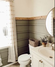 a white toilet sitting next to a bathroom sink under a round mirror in a bathroom