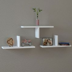 two white floating shelves with pictures and flowers on them, one shelf has a small plant