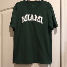 Miami Graphic T-Shirt. Unisex. Size Large Pit To Pit When Laying Flat 21" Length From Shoulder 29 1/2" Preowned In Great Shape! Looks Unworn. Tan Crew Neck Top With Text Print, Casual Tan Tops With Text Print, Casual Tan Top With Text Print, Green Collegiate T-shirt With Letter Print, Green College Fan Apparel T-shirt, Collegiate Green Letter Print T-shirt, Casual Green Top With Text Print, Collegiate Green Tops With Logo Print, Collegiate Green Top With Logo Print