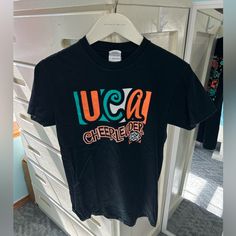 Uca Universal Cheerleading Association Cheerleader T-Shirt Tee Shirt 100% Cotton By Varsity Cheersize Small! Brand New! Bought From A Camp As A Camper Years Ago!! Now As A Uca Camp Staffer I’m Letting A Bunch Of Cheer Things Go!! Check Out The Rest Of My Closet!! Black Fan Gear T-shirt With Text Print, Black T-shirt With Text Print For Fans, Black T-shirt With Team Name For Cheerleading, Black Crew Neck T-shirt For Cheerleading, Orange Cotton T-shirt For Game Day, Black Sports Fan T-shirt For College, Black College Sports Fan T-shirt, Orange Short Sleeve Team Spirit Top, Black Crew Neck T-shirt For School Spirit